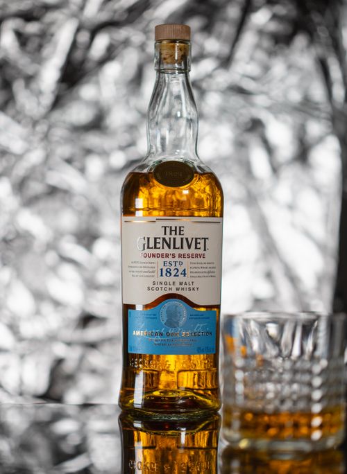 Free Close-up of The Glenlivet Founder's Reserve whiskey bottle with glass on reflective surface. Stock Photo
