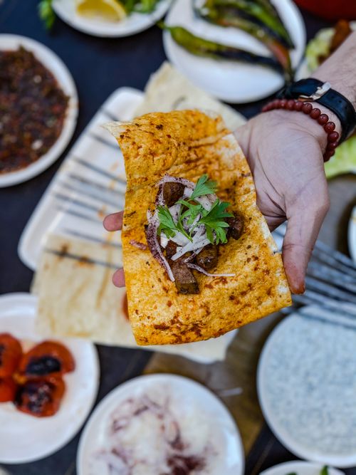 Free A flavorful meat wrap with onions and greens, held over various side dishes, creating a savory dining atmosphere. Stock Photo