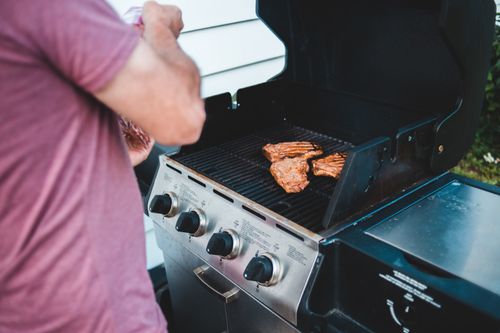 Free Man grilling steaks on an outdoor gas barbecue, showcasing delicious food preparation. Stock Photo