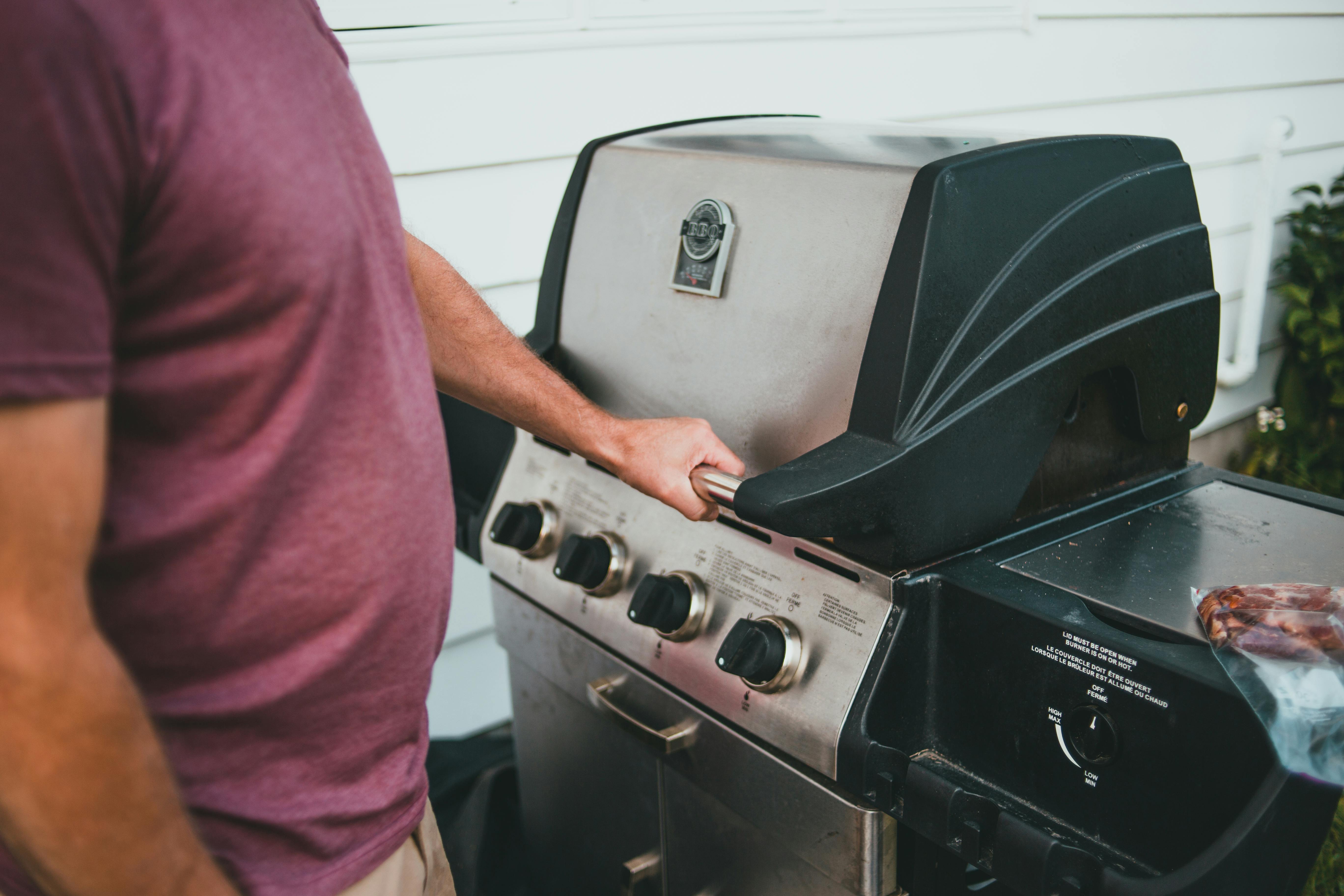 Adult man using a gas grill for outdoor cooking. Perfect summer barbecue scene.