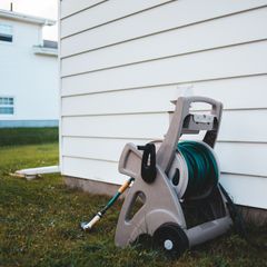Grey free-standing hose reel with a green hose wound on it, on a lawn beside a white clapboard house