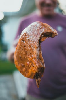 Close-up of a juicy grilled steak held on a fork outdoors with a blurred background.
