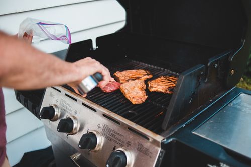 Free A man seasons steak on a grill for a backyard barbecue, displaying outdoor cooking. Stock Photo