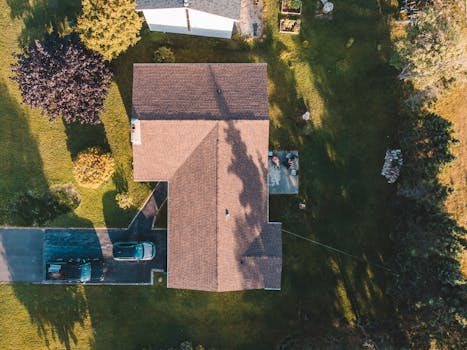 Drone shot capturing a suburban house with parked cars and a green lawn.