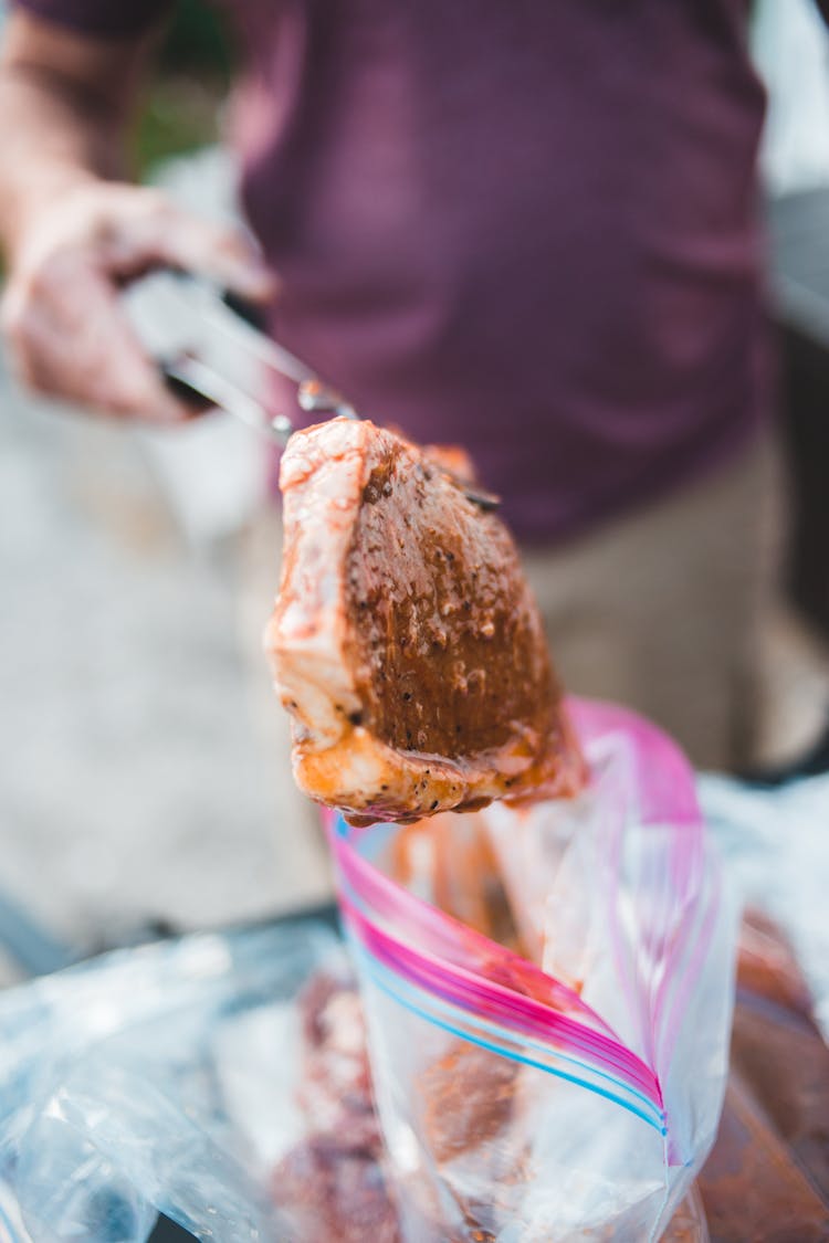 Person Holding A Marinated Pork On Tongs