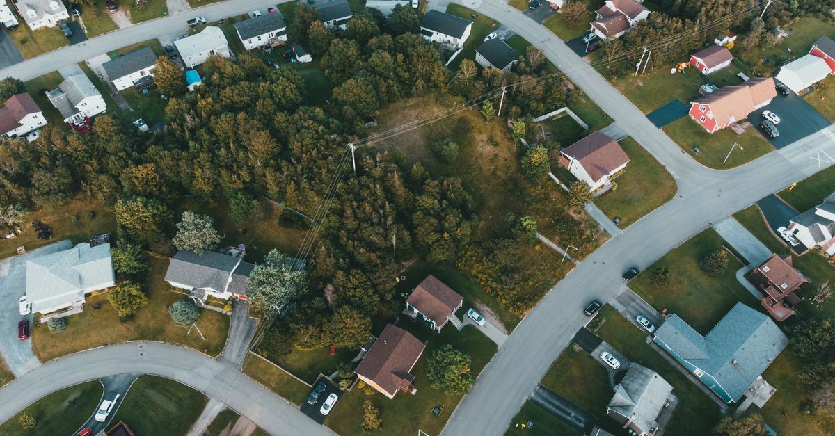 Aerial shot of a suburban neighborhood with houses and lush greenery, captured during the day.