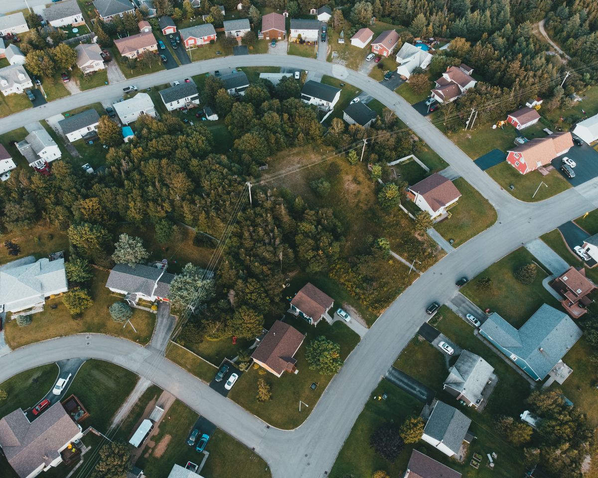 Aerial shot of a suburban neighborhood with houses and lush greenery, captured during the day.