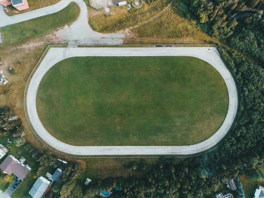 Drone shot of a green sports field surrounded by trees and buildings, perfect for athletics.