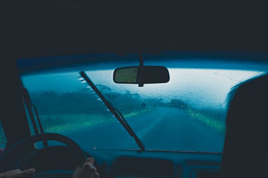 View from car interior during a rainy journey, emphasizing wet windshield and dim surroundings.
