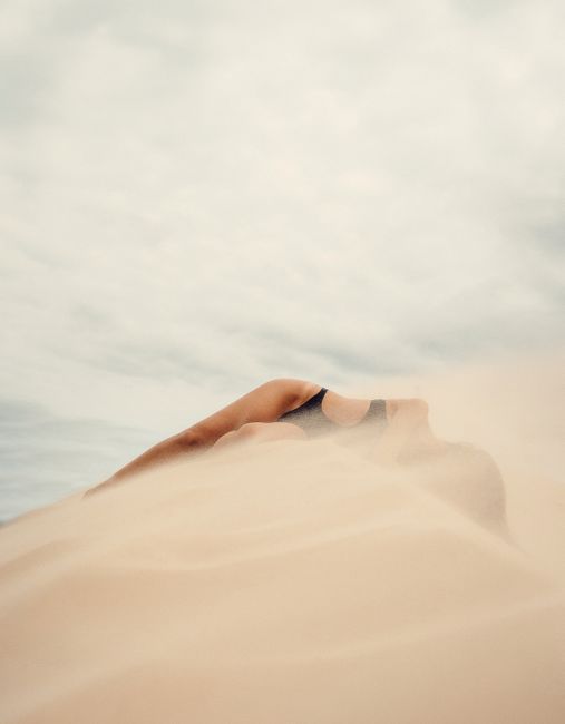 A tranquil beach scene in Brazil with a woman lying on sandy dunes under a cloudy sky.