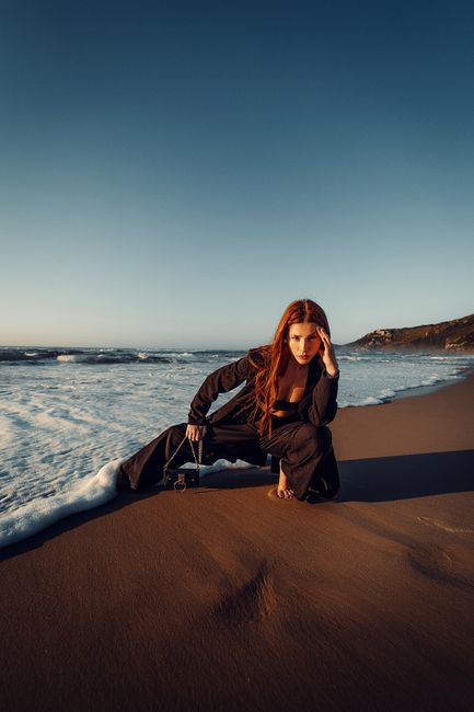 Fashionable woman in chic black outfit posing on a picturesque beach during sunset in Florianópolis, Brazil.