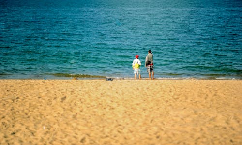 무료 해변 근처에 서있는 두 사람 스톡 사진