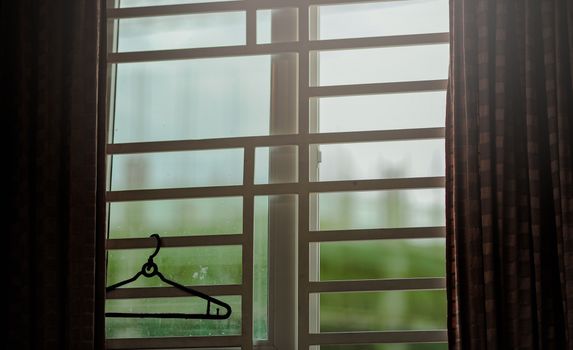 Quiet interior scene showing a view through a window with a clothes hanger and curtains.