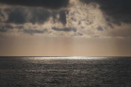 Free A dramatic seascape with dark clouds above a tranquil ocean at twilight, creating a serene atmosphere. Stock Photo