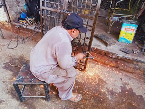 Free Man Sitting on a Stool While Repairing a Gate Stock Photo
