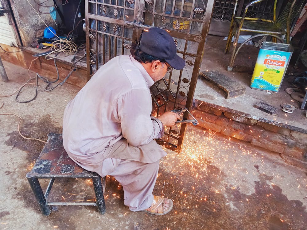 Man Sitting on a Stool While Repairing a Gate