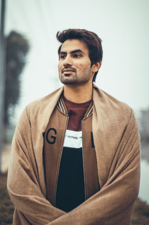 Free Portrait of a man in a jacket and scarf, looking thoughtful outdoors. Stock Photo