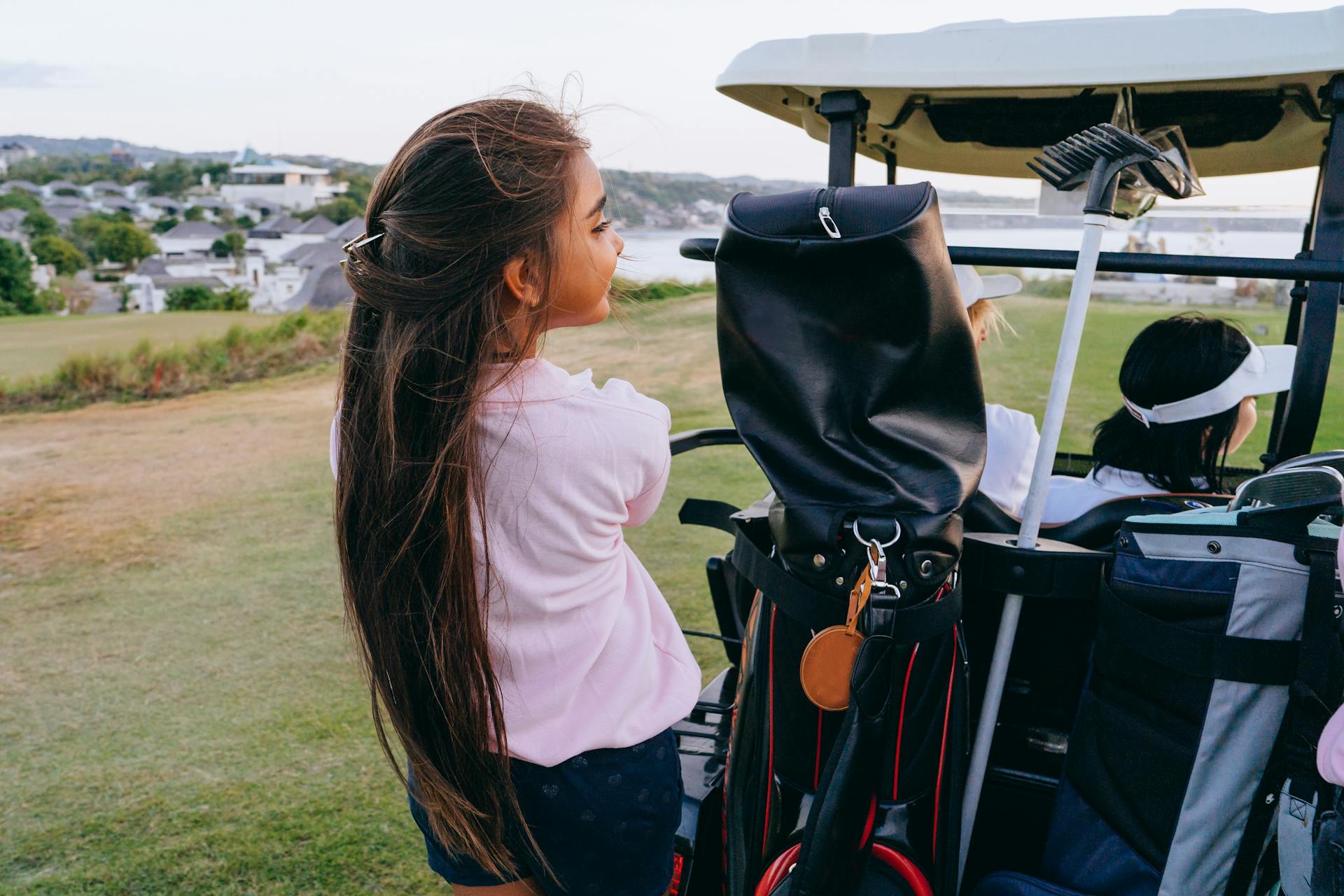 A young girl with long hair sits in a moving golf cart enjoying a scenic view.