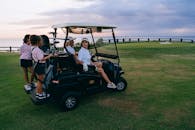 在海边的日落时分，家人和朋友在休闲高尔夫郊游期间乘坐高尔夫球车