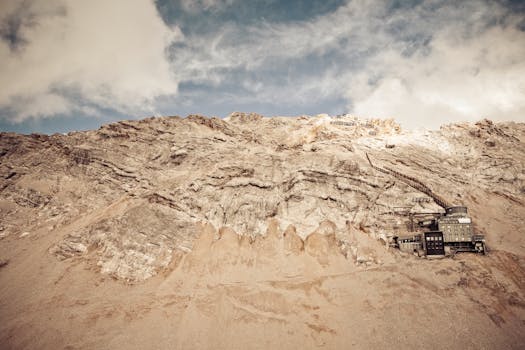 Dramatic view of a rocky mountainside with clouds and a small remote building.