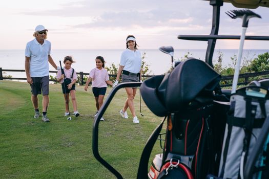 A family having fun on a golf course during a sunny day with golf equipment in view.