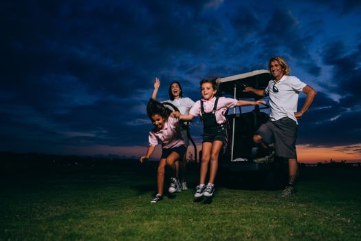 A family enjoying a fun golf outing with kids playing and adults smiling at sunset.