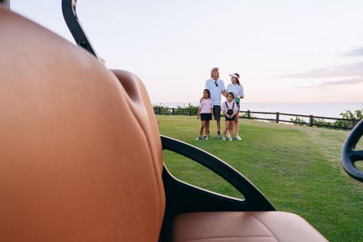 A family enjoys a day on the golf course with a beautiful sunset background.