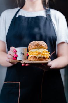 Person in apron holding a delicious breakfast sandwich and coffee cup.