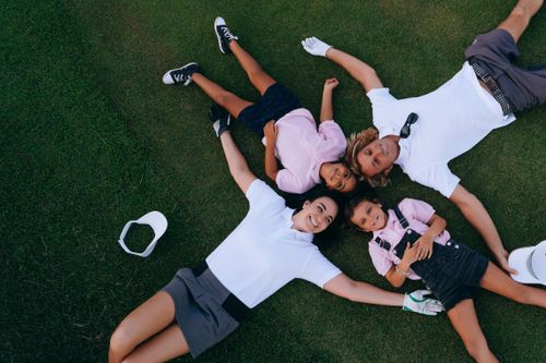 Free A joyful family of four lying on a golf course lawn, smiling and embracing. Stock Photo