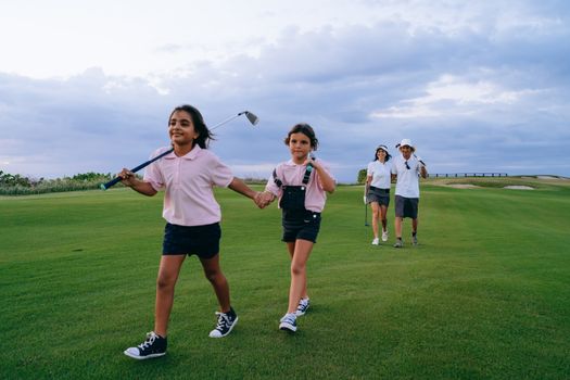 A family enjoys bonding outdoors on a lush golf course holding golf clubs.