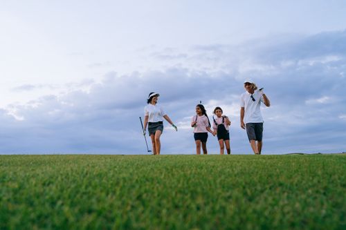 Free A family of four walking together on a golf course with golf clubs, enjoying the outdoors. Stock Photo