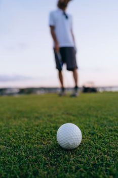 Golf ball on green grass with a player blurred in the background at a golf course.