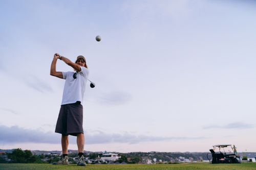 Free A man swinging a golf club on a scenic outdoor course during the evening. Stock Photo