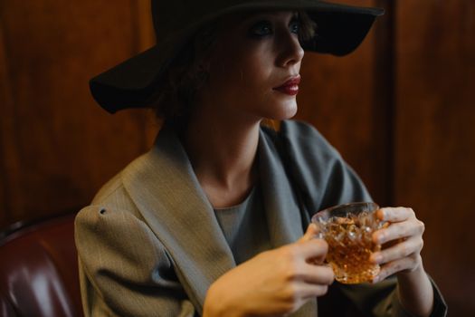A stylish woman in a hat enjoys a drink indoors, exuding elegance.