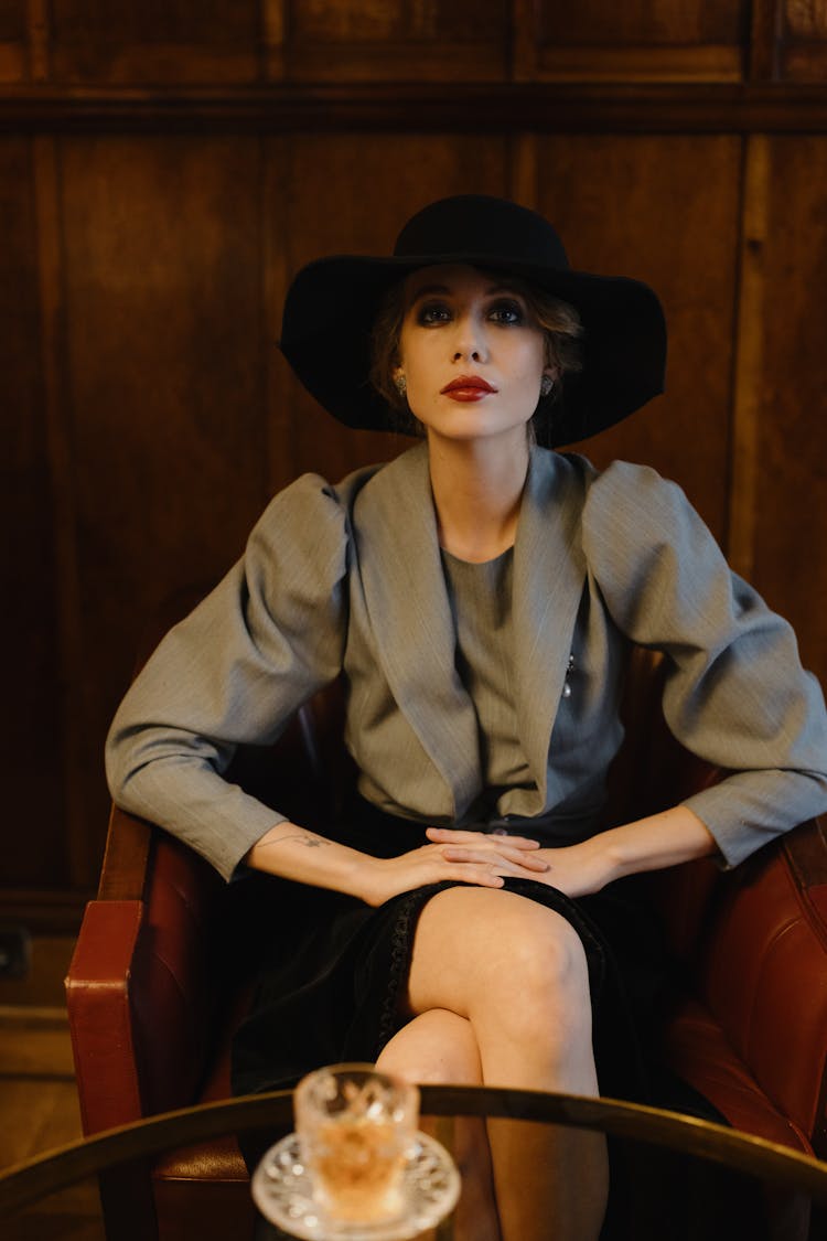 A Woman With A Black Hat Sitting On A Chair