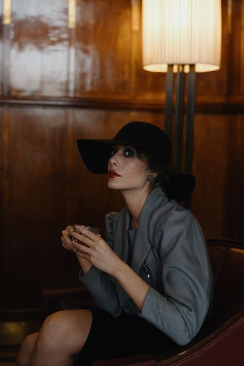 Free A sophisticated woman in a black hat enjoys a drink in an upscale setting. Stock Photo
