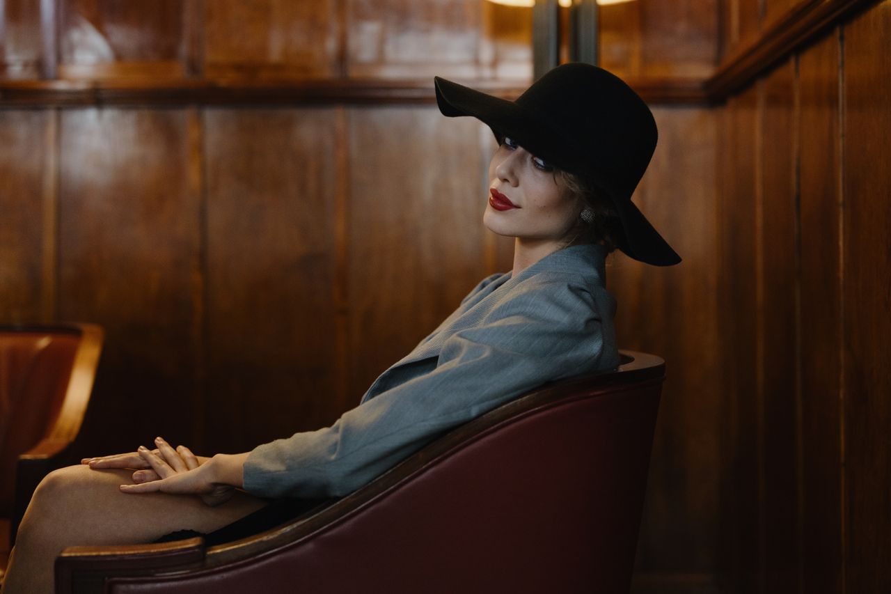 stylish woman with red lips and wide brimmed hat sitting indoors with