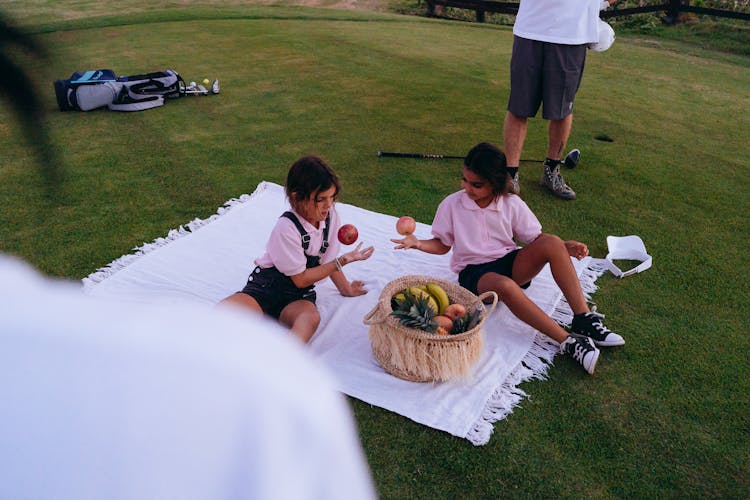 Cute Girls Sitting On White Picnic Blanket