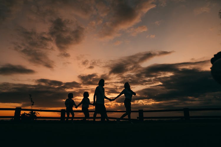 

A Silhouette Of A Family Walking While Holding Hands