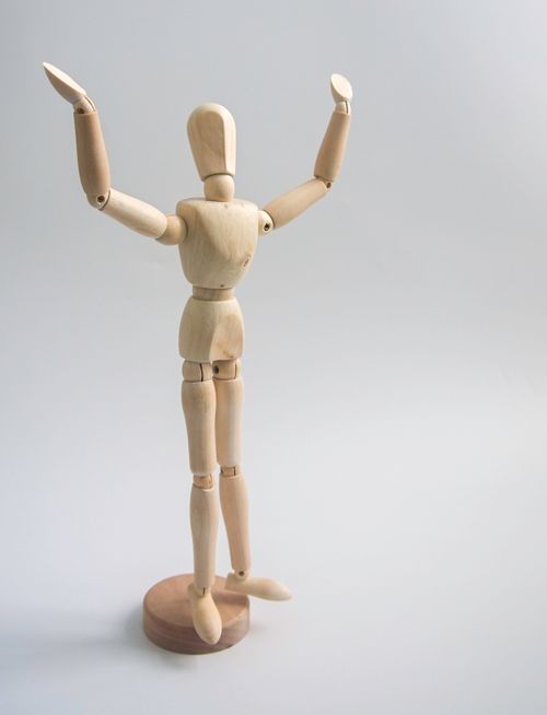 Free Wooden mannequin figure with raised arms on a plain grey background, symbolizing success and creativity. Stock Photo