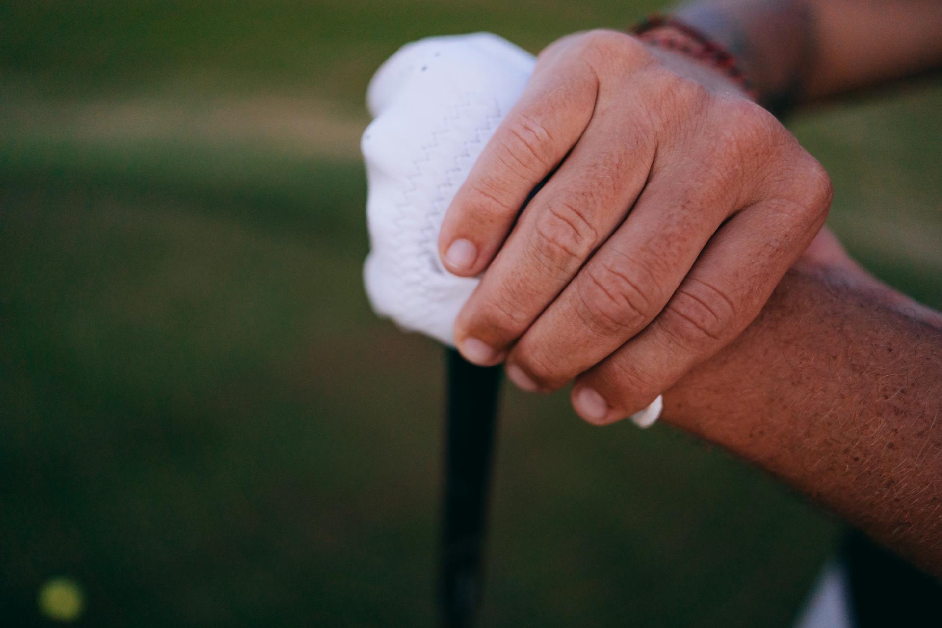 Detailed view of hands gripping a golf club with a white glove outdoors.