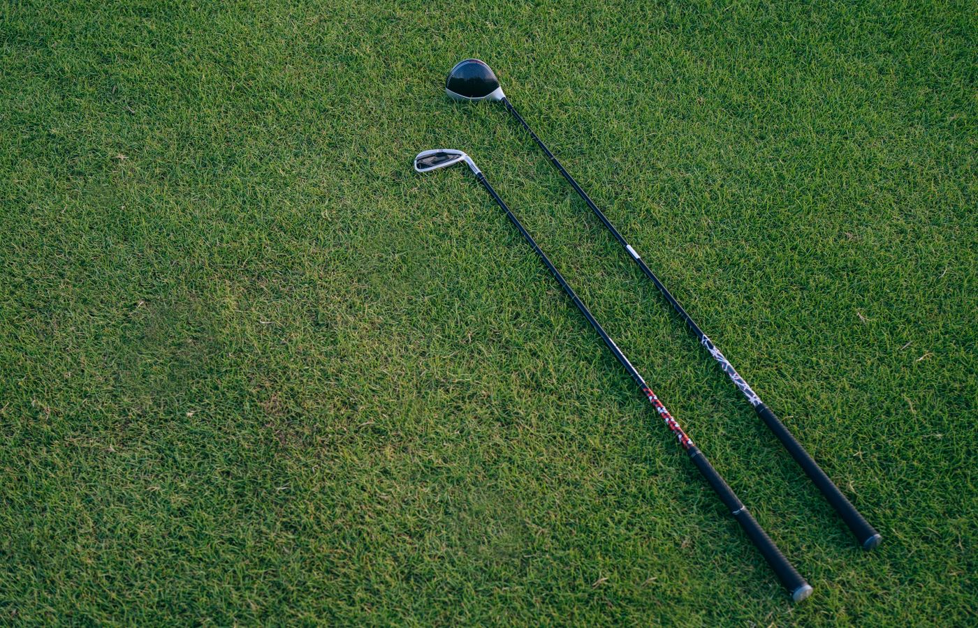 Two golf clubs lying on a lush green golf course, ideal for golfing enthusiasts.