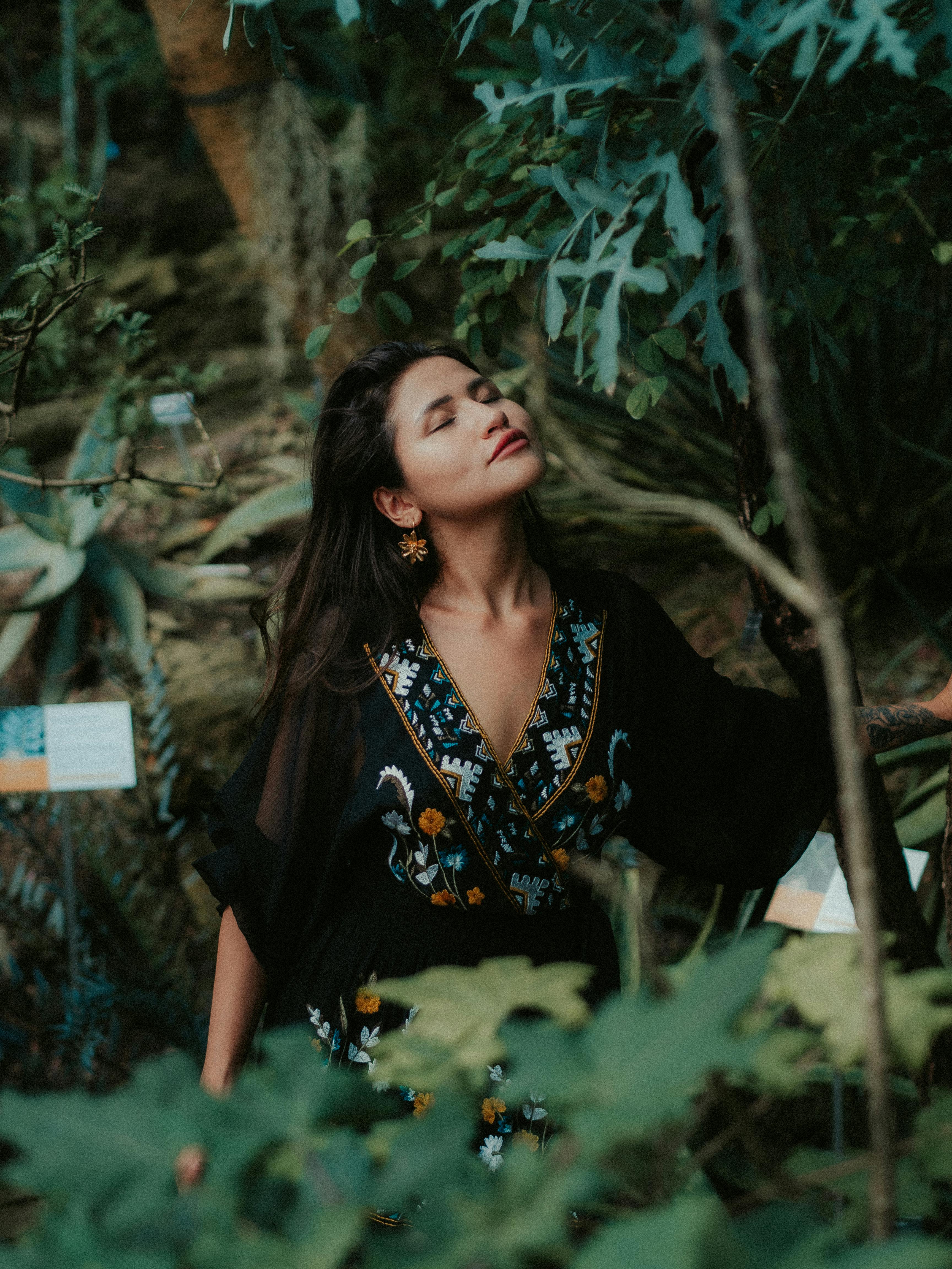 A woman in a black embroidered dress embraces tranquility amidst lush greenery.