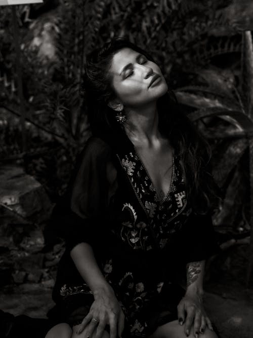 A Grayscale Photo of a Woman in Black Dress Sitting with Her Eyes Closed