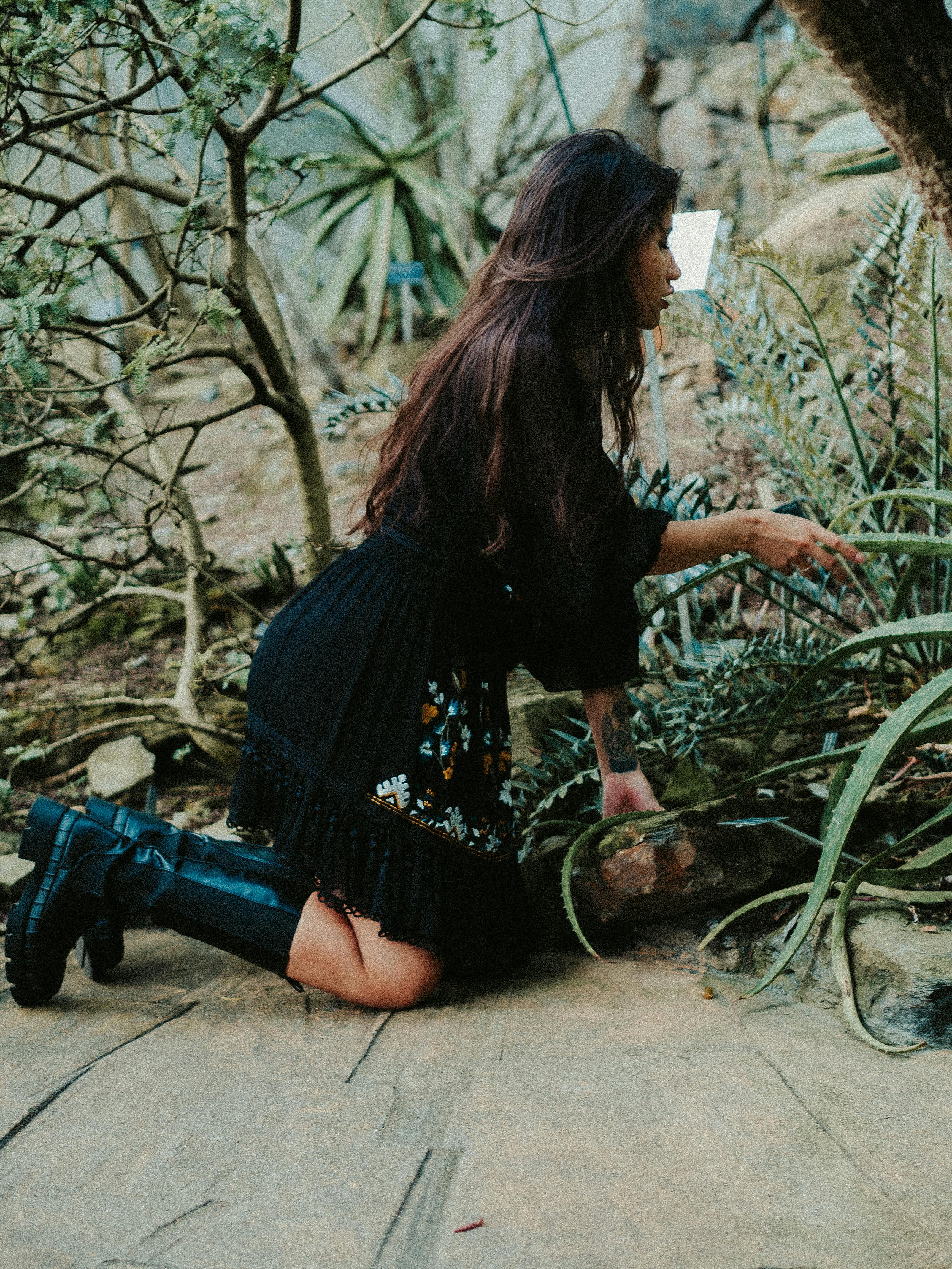 A woman in a black dress explores a lush garden, surrounded by greenery and plants.