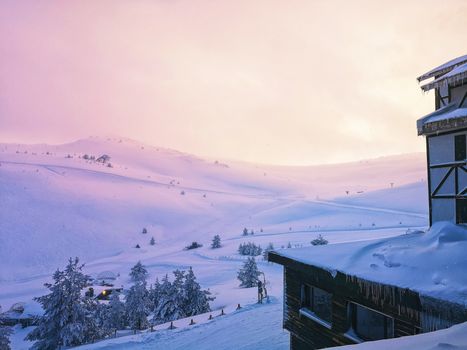 Peaceful winter landscape with snowy mountains and a building at sunset.