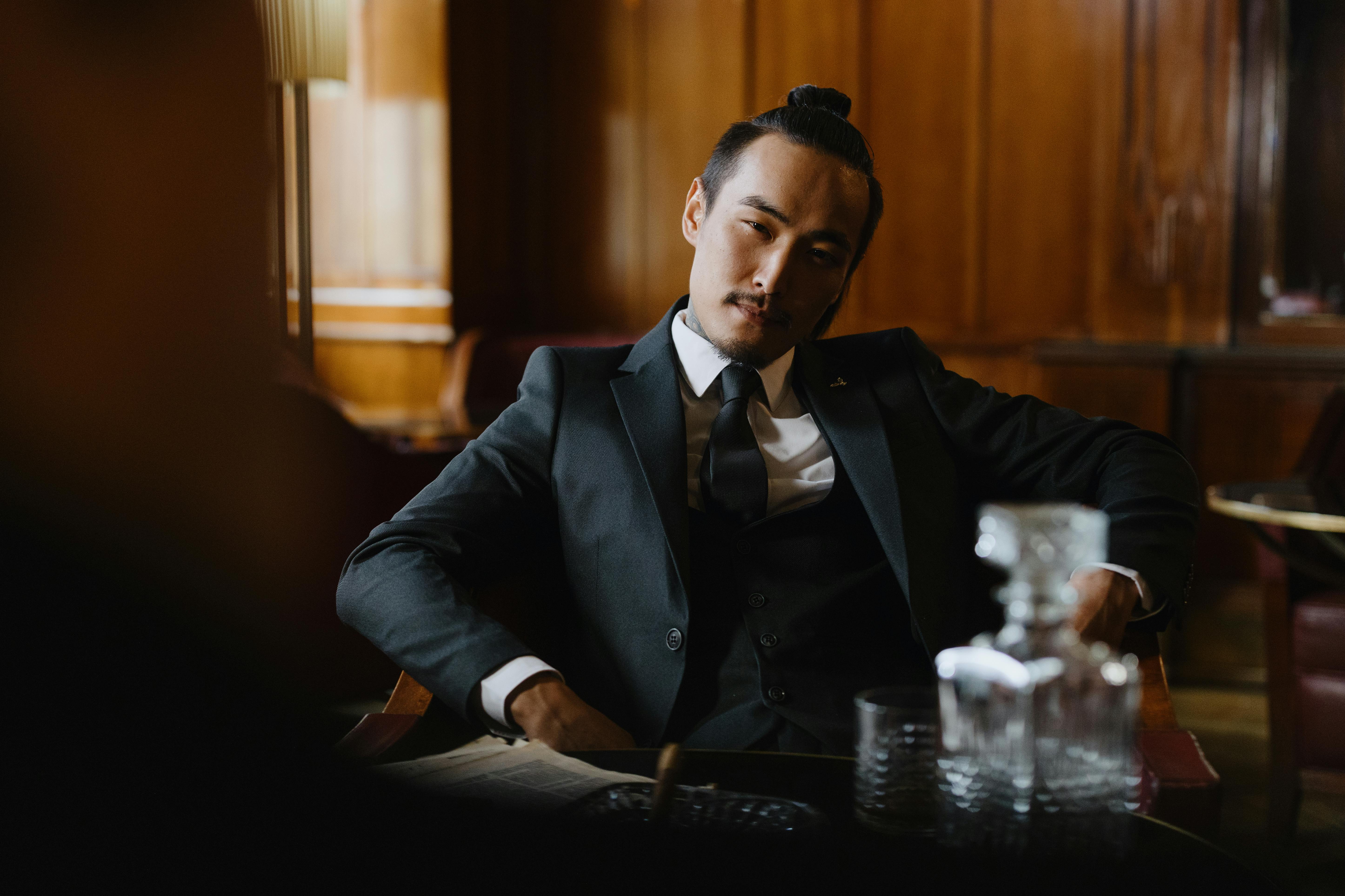 Elegant man in formal attire seated in a classic wood-paneled lounge, exuding sophistication.