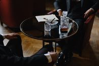 Men in Black Suits Sitting on Armchairs Beside Round Table with Pitcher and Glass