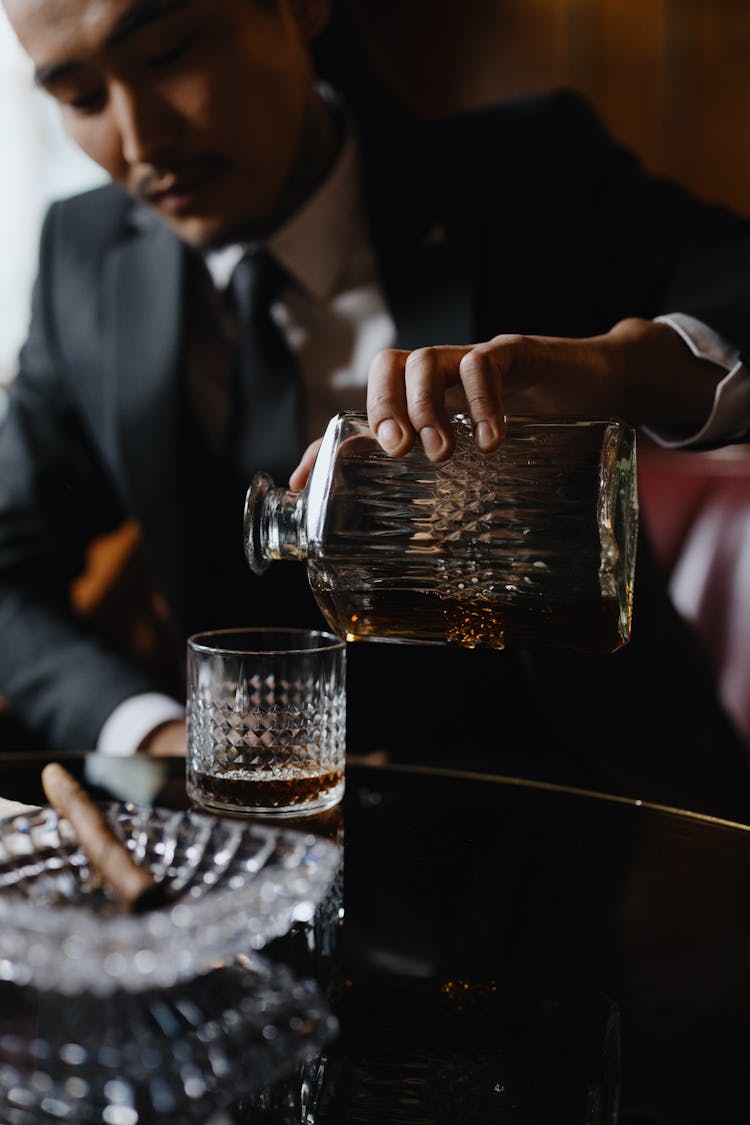 A Man In A Suit Pouring Whiskey From A Decanter