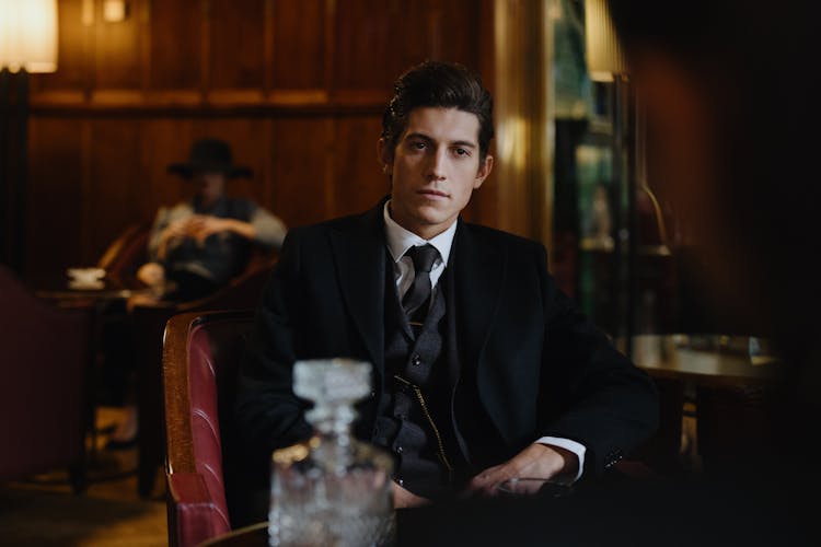 Man In Black Suit Sitting On Red Leather Chair